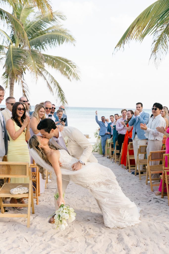 A newlywed couple kissing as they leave their ceremony with the Caribbean Sea in the background in Playa del Carmen